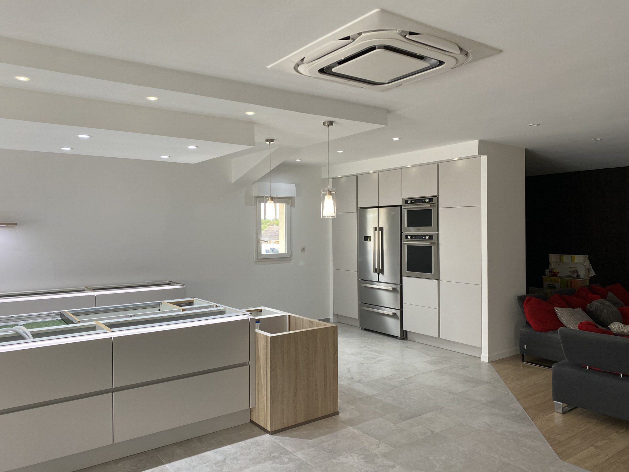 Cuisine en pose avec îlot central, électroménagers modernes et sol carrelé gris.
