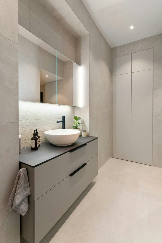Salle de bain moderne avec vasque blanche et meuble gris. ABM France, cuisiniste normandie.